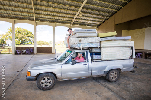 Two men riding on loaded truck help to move mattresses at orphanage.
