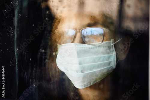 Woman looking through the wet window during stay home while COVID-19