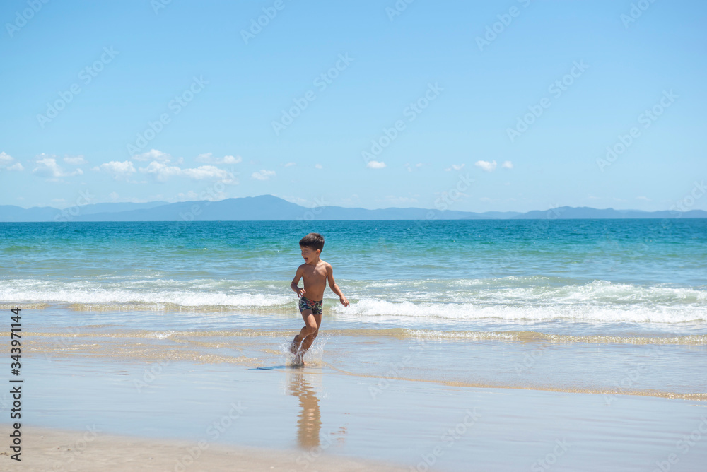 Little boy running on beach beside blue sea in a sunny day of summer.