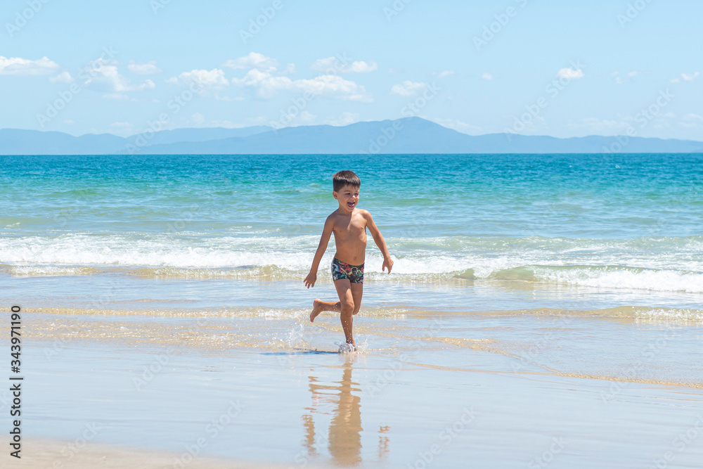 Little boy running on beach beside blue sea in a sunny day of summer.