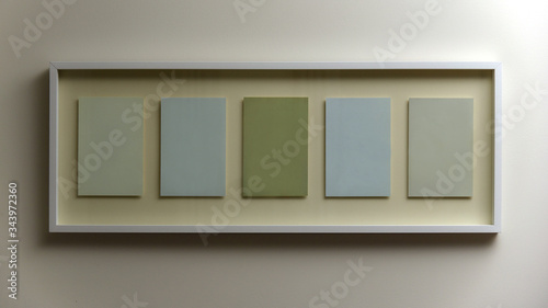 Frame hanging on wall with five empty spaces in green and blue colours © Brett