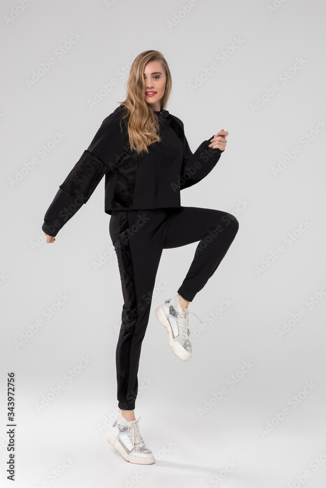 Obraz premium cute blonde girl posing in chic long sleeve black sports wear. white sneakers. white background.