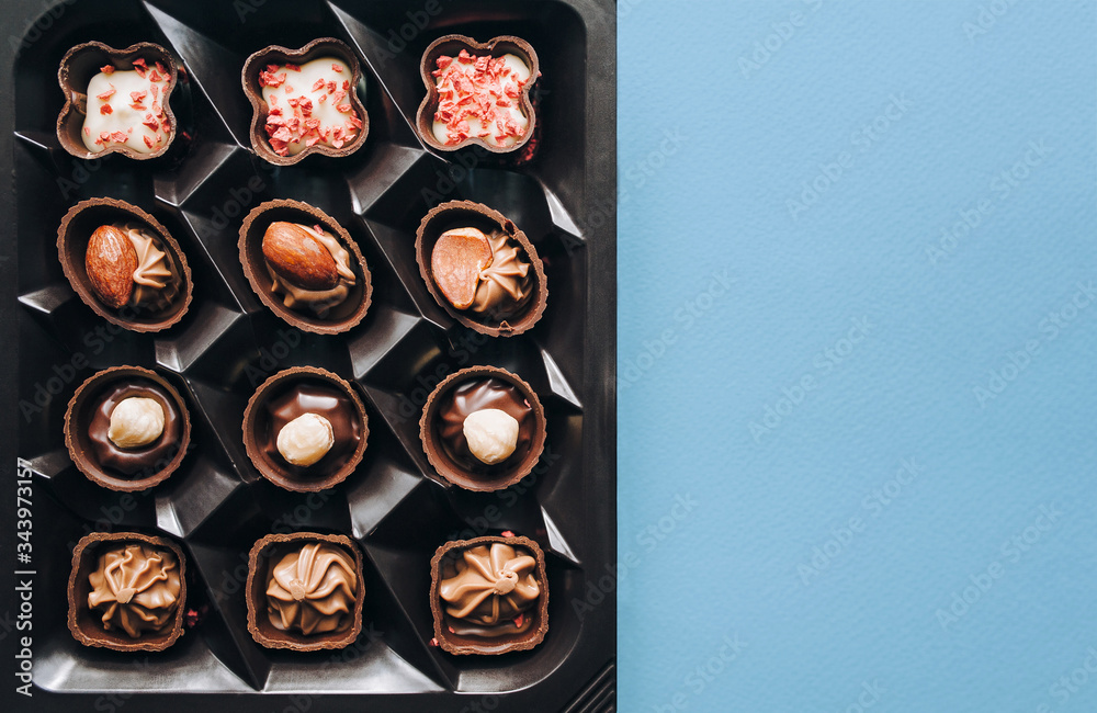 Box of beautiful chocolate candy with nuts on a blue background, top view with copy space.