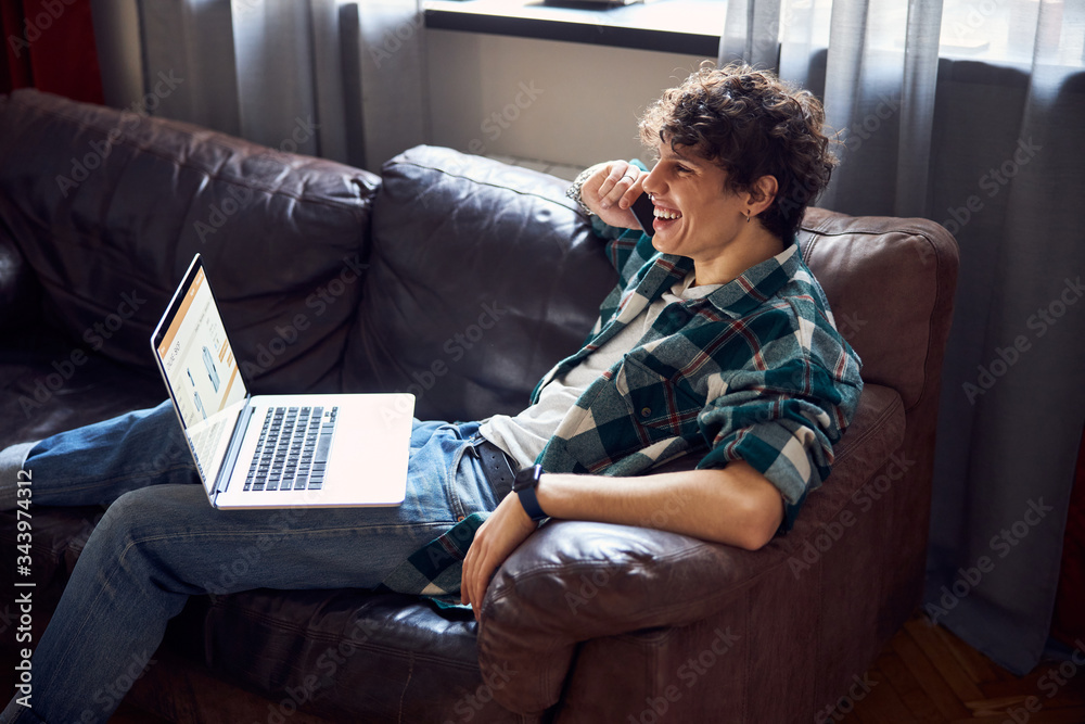Cheerful young man resting on couch and talking on cellphone Cheerful young man resting on couch and talking on cellphone