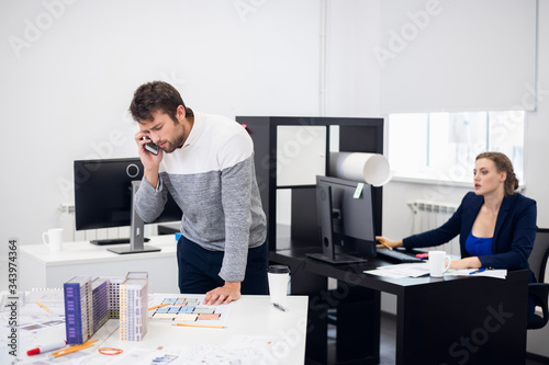 A construction engineer is solving some questions over the phone, while his colleague is working on her computer in the background