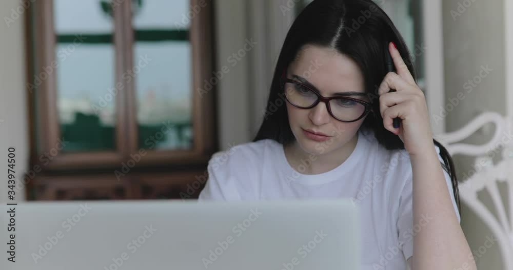 Thoughtful student in glasses working with laptop and frazzles head at table