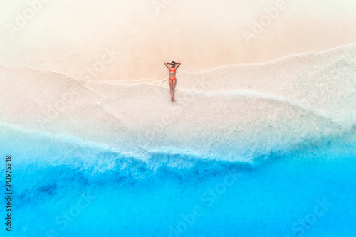 Aerial view of the beautiful young woman lying on the white sandy beach near sea with waves at sunset. Summer travel. Top view of slim girl, transparent blue water. Indian Ocean in Zanzibar, Africa © den-belitsky