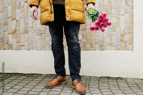 blond man in a yellow winter jacket with a bouquet of tulips in hands photo