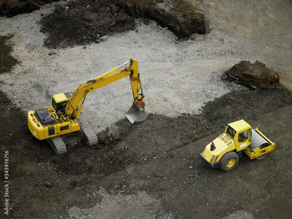 Aerial shot of steamroller and earth mover on building plot Aerial shot of steamroller and earth mover on building plot