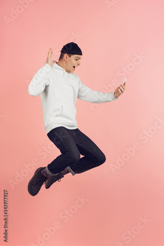Selfie, video call. Caucasian young man's modern portrait isolated on pink studio background. Beautiful male model in high jump. Concept of human emotions, facial expression, sales, ad. Copyspace.