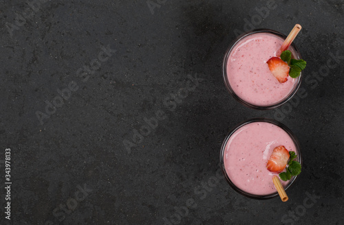Strawberry smoothie with granola and nuts in a glass with a bamboo straw on a dark background top view