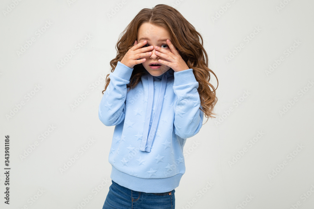 European teenage girl in a blue hoodie covered her eyes with her hands on a white background with copy space European teenage girl in a blue hoodie covered her eyes with her hands on a white background with copy space