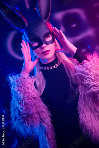 sexy girl in a bodysuit and fur coat with a rabbit mask in the neon light