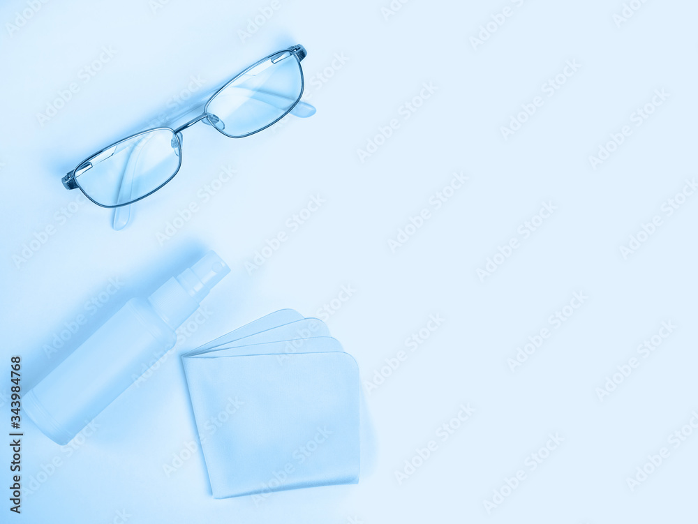 Glasses care product. Glasses, spray, napkin for glasses on light background. Blue monochrome background. Ophthalmology Glasses care product. Glasses, spray, napkin for glasses on light background. Blue monochrome background. Ophthalmology