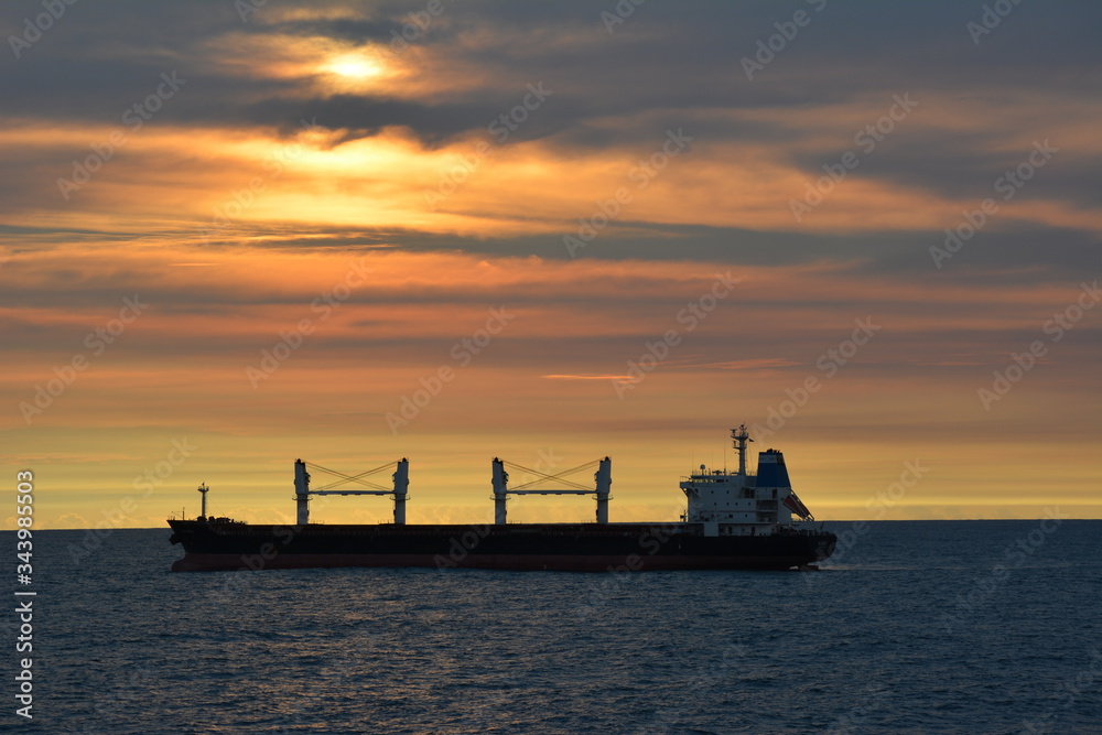 A cargo ship silhouetted against a setting sun sky. A cargo ship silhouetted against a setting sun sky.