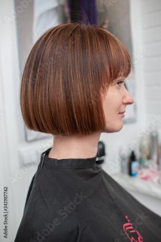 Canvas Haircut bob on bright mahogany hair of a young woman in a beauty salon