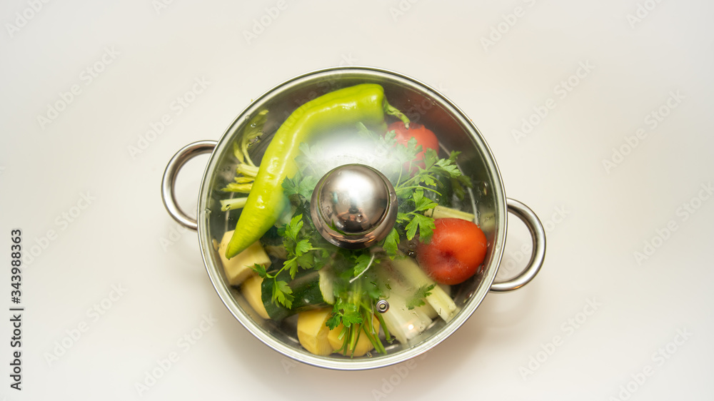 
Steel pot, filled with various vegetables and covered with a glass lid, close-up