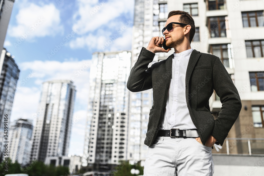 Successful young businessman in a smart casual speaks on the phone among the skyscrapers, sunglasses on it Successful young businessman in a smart casual speaks on the phone among the skyscrapers, sunglasses on it