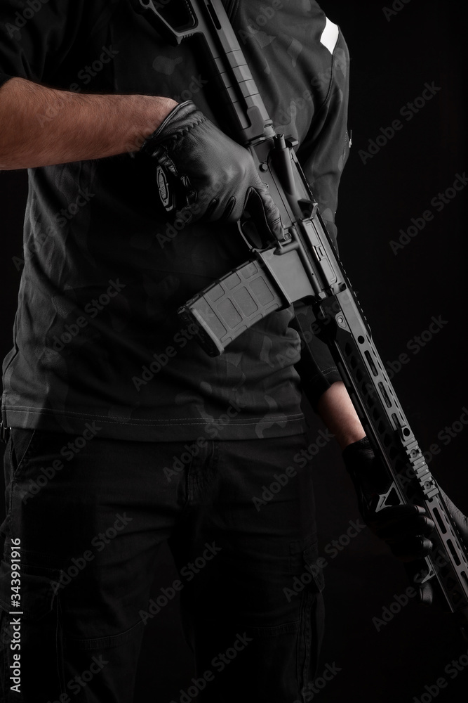 A man holds an automatic carbine on a dark back. A fighter in dark clothing with a weapon in his hands. Poster concept for police, security or military. A man holds an automatic carbine on a dark back. A fighter in dark clothing with a weapon in his hands. Poster concept for police, security or military.