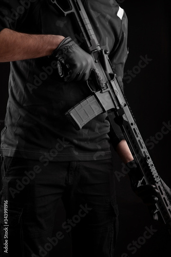 A man holds an automatic carbine on a dark back. A fighter in dark clothing with a weapon in his hands. Poster concept for police, security or military.