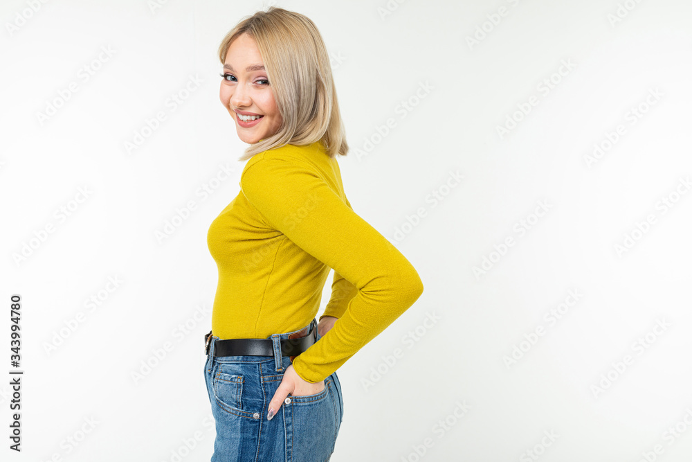 blond girl in a tight-fitting yellow jacket and jeans posing sideways on a white background blond girl in a tight-fitting yellow jacket and jeans posing sideways on a white background