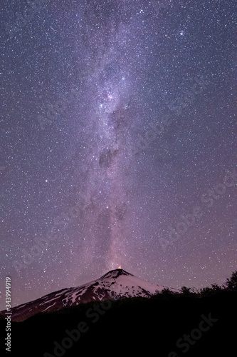 Thousands of stars in the sky with the Milky Way above the Villarrica Volcano in Chile with silhouettes of some trees, vertical photo