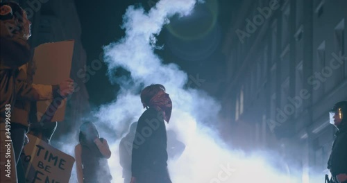 Group of activists participate in the movement to end gun violence. Male protestor throwing the smoke grenade over security force standing on the street at night.
 photo