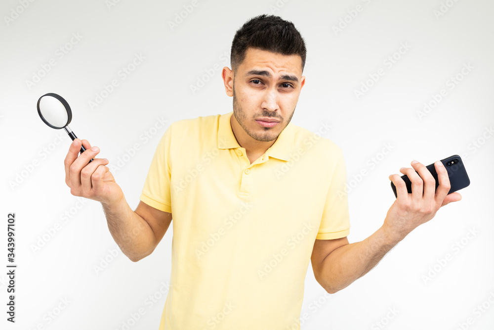 handsome man with low vision holds a magnifier and a smartphone in his hand on a white background with copy space handsome man with low vision holds a magnifier and a smartphone in his hand on a white background with copy space
