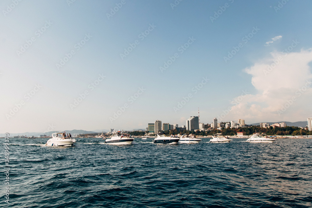White luxury yachts and boats sail in a row on the open sea against the background of the city