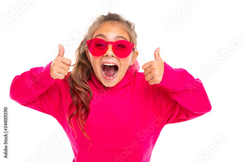Fashionable teenager girl in pink hoody and with pink sunglasses gesticulates, portrait isolated on white background
