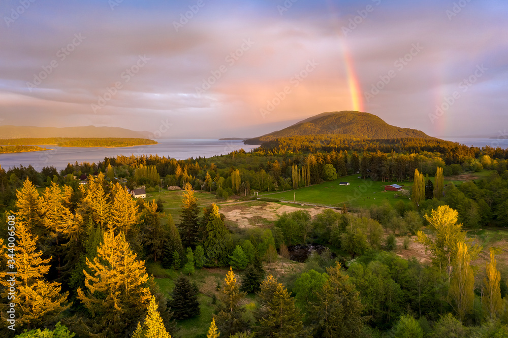 Aerial View of a Beautiful Island Sunset With a Gorgeous Rainbow. Springtime brings dramatic sunsets and colorful rainbows but hardly ever both. This is Lummi Island, Washington in the Salish Sea.