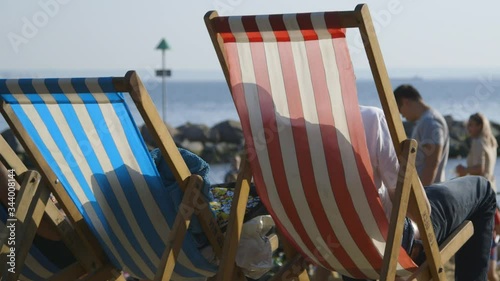People relaxing on red and white and blue and white striped deckchairs on a British beach in summer
