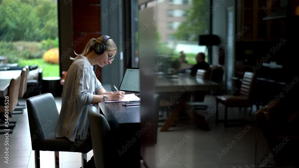 Female employee having overtime work sitting at table and editing financial reports connected to 4g wireless on laptop computer for listening music via electronic headphones for noise cancellation
Female employee having overtime work sitting at table and editing financial reports connected to 4g wireless on laptop computer for listening music via electronic headphones for noise cancellation