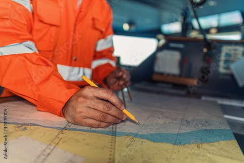 Filipino deck Officer on bridge of vessel or ship wearing coverall during navigaton watch at sea . He is plotting position on chart photo