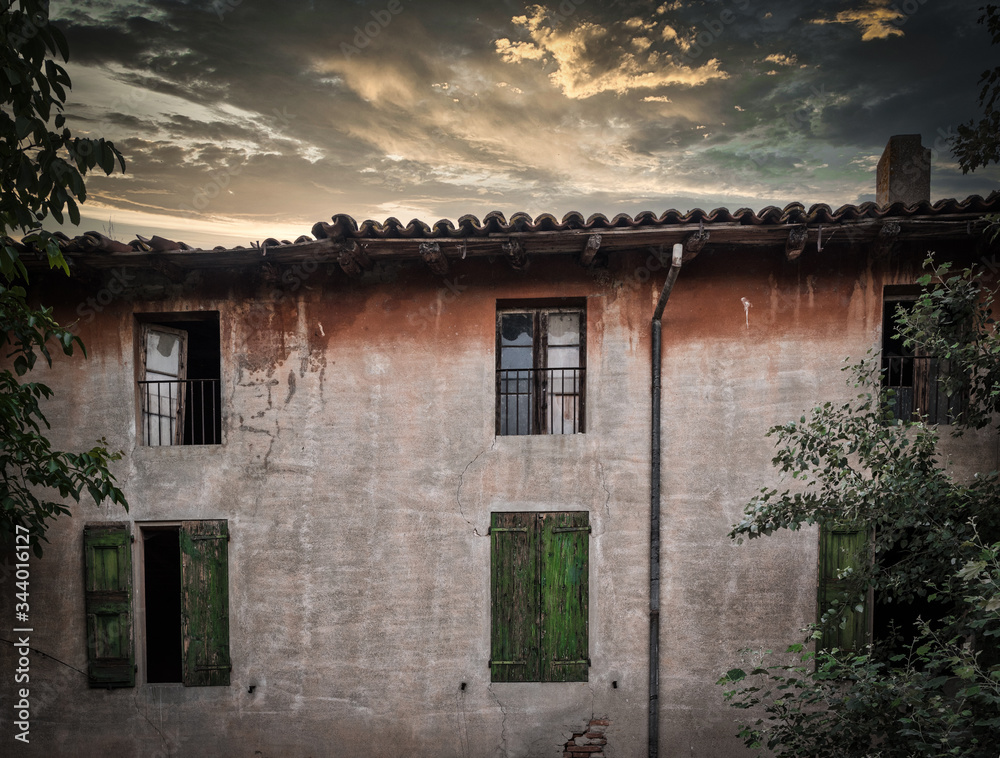 Rundown building with green shutters at sunset under stormy clouds Rundown building with green shutters at sunset under stormy clouds