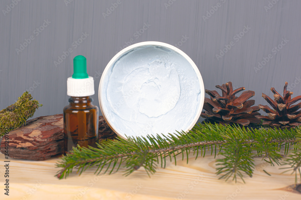 ecological body care cosmetics, body scrub and essential oils, pine cones and twig on a gray background