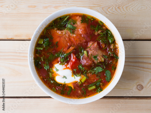 Borsch with sour cream in a white bowl on a wooden background. Top view