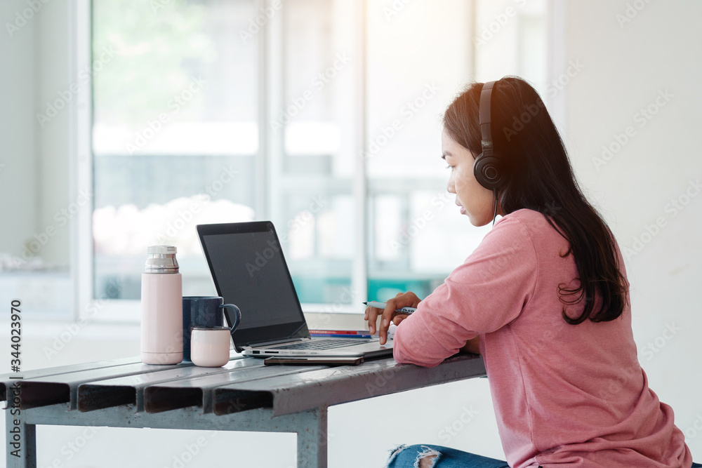 Portrait of a young Asian female adult learner studying online at home during Coronavirus or COVID-19 pandemic. Businesswoman work with laptop at home in house corridor and garden Portrait of a young Asian female adult learner studying online at home during Coronavirus or COVID-19 pandemic. Businesswoman work with laptop at home in house corridor and garden