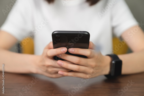 Closeup of young woman hand holding smartphone and chatting with friends at social network on the table in cafe.