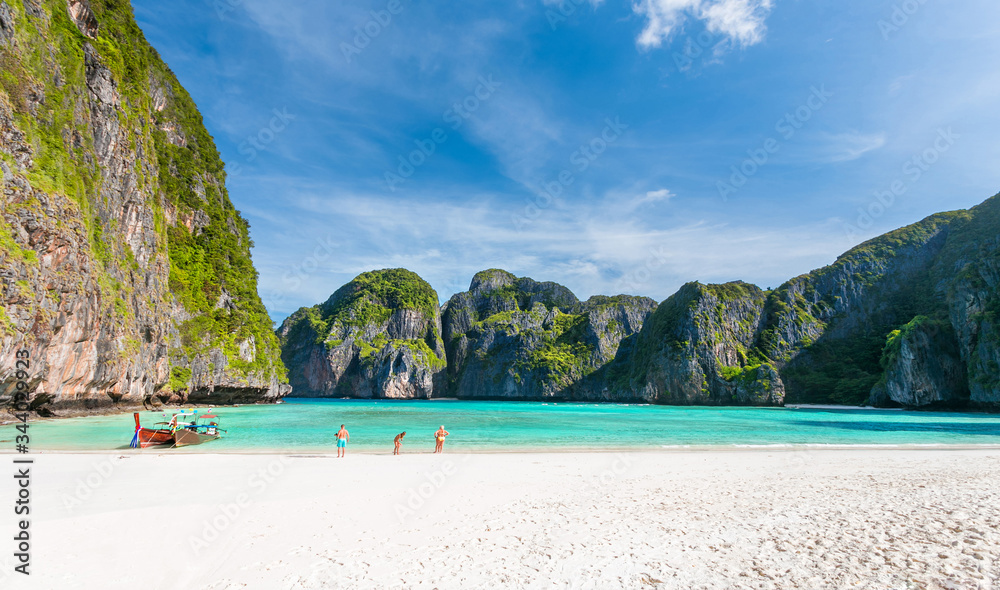 Obraz premium Beautiful tropical beach with white sand and turquoise ocean against blue sky with clouds on sunny summer day at Phi Phi island. Travel vacation background for relaxing vacation island of Thailand.
