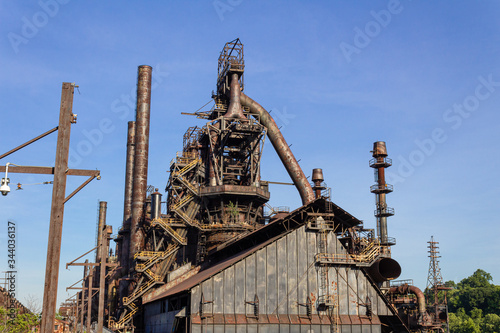 Massive industrial complex, abandoned and weathered furnaces and smokestacks before a deep blue sky, horizontal aspect