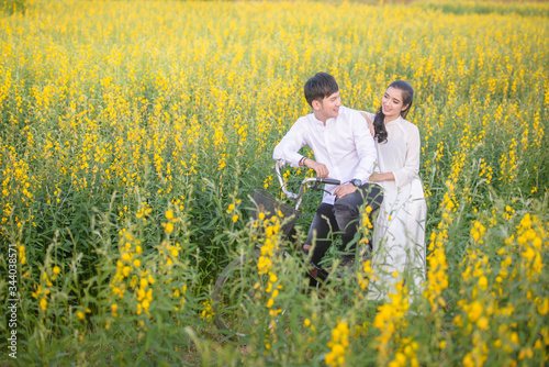 Asian Couples  are walking and biking in the field of Crotalaria juncea flowers happily. Concept portrait pre-wedding.
