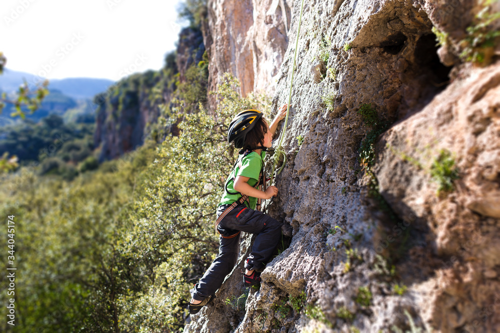 The child in helmet is climbing on a natural terrain.