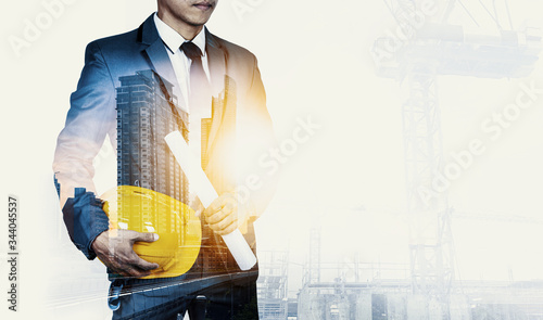 Double exposure image of engineer holding safety helmet with city view and construction site.The boss have vision and leadership for strategy in business to success in market mechanism concept.