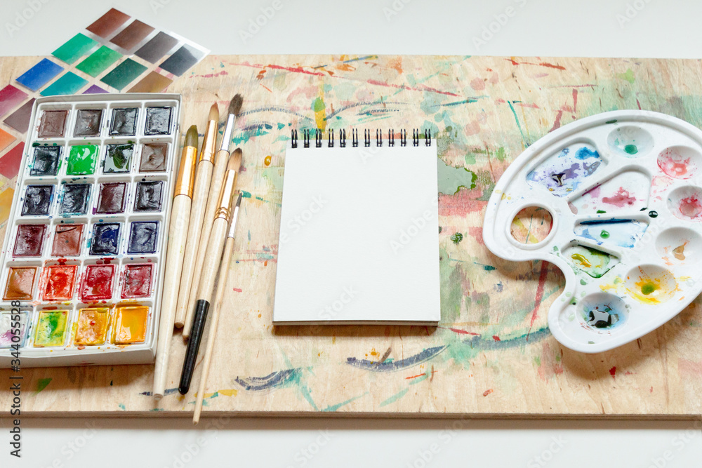 Set of watercolor paints, art brushes, palette and empty sketchbook. Art creativity concept.