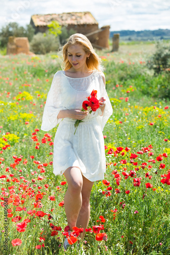 Woman  in white dress walking and holding bouquet of poppies plants