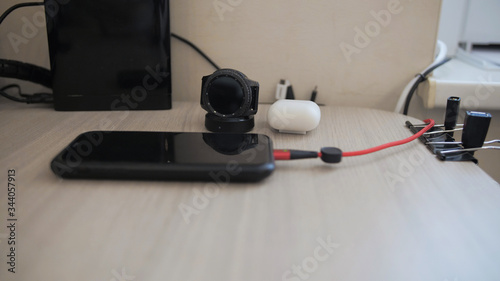 Black phone with a red wire black watch and a case with headphones on the table