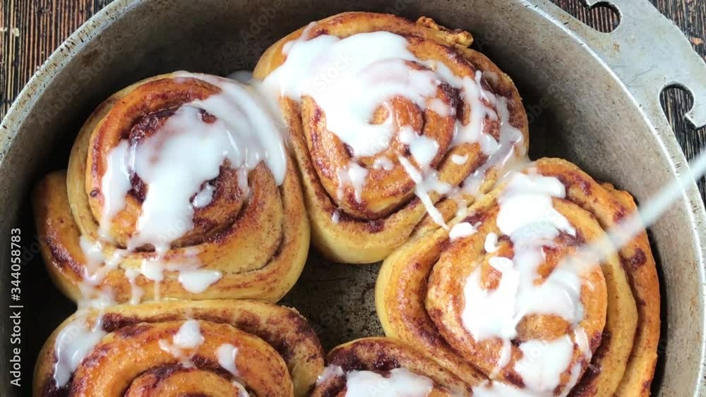 drizzling with white sugar glaze over top of baked cinnamon rolls in pan flat lay drizzling with white sugar glaze over top of baked cinnamon rolls in pan flat lay