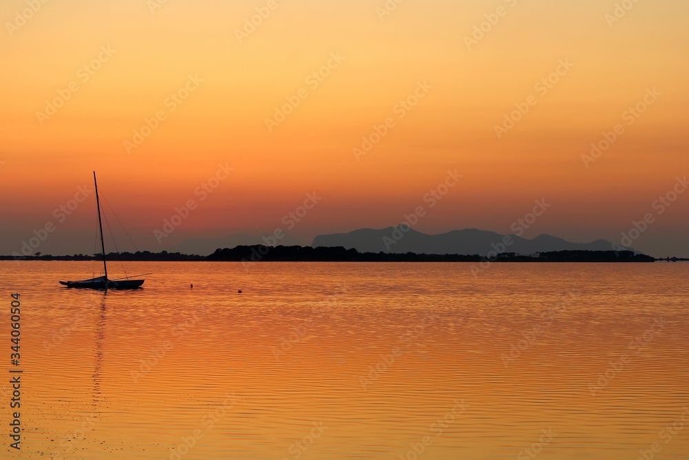 sailboat moored on the sea at sunset and headland on the background