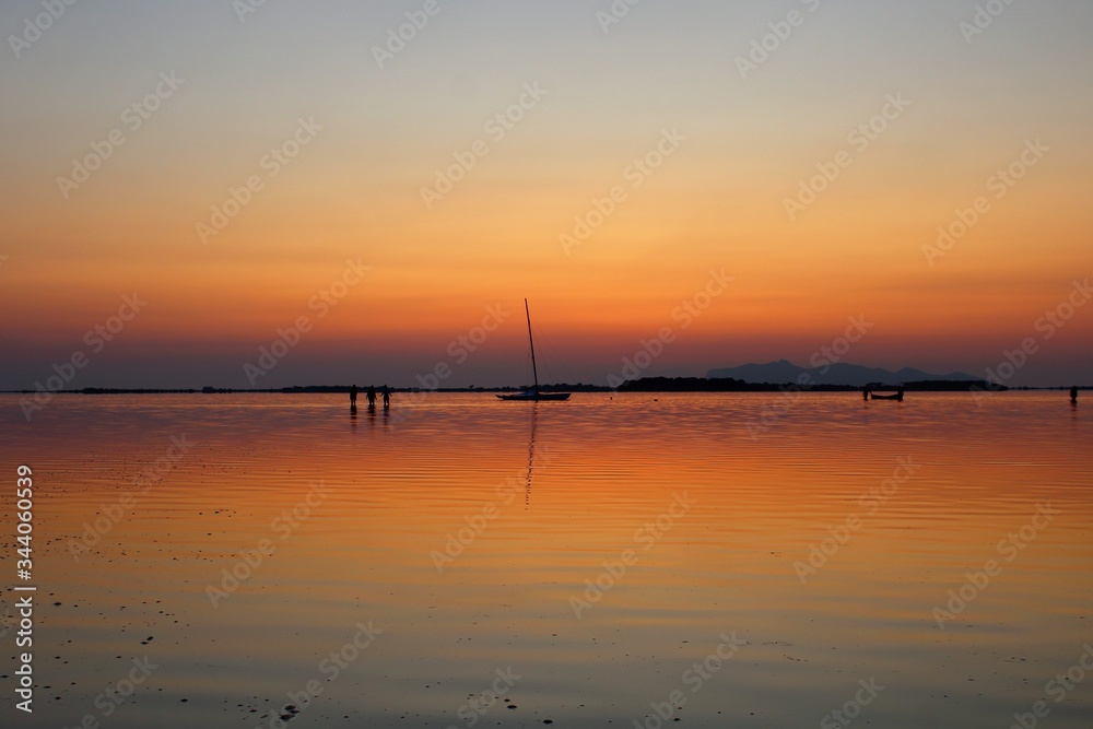 sailing boat and canoe moored on the sea at sunset and headland on the background